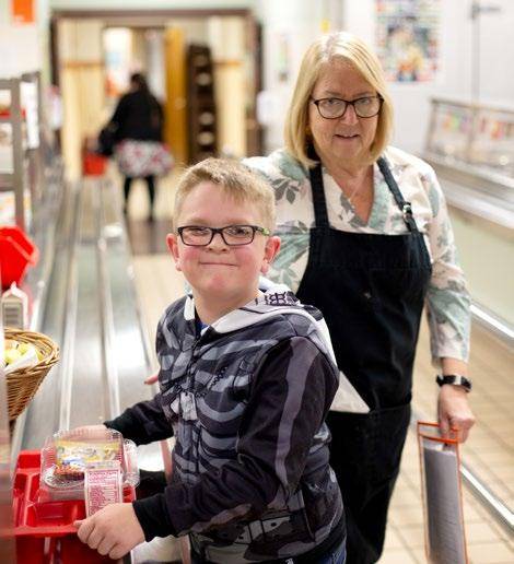 Student is holding a red tray in the cafeteria line and a food service provider is in the background.